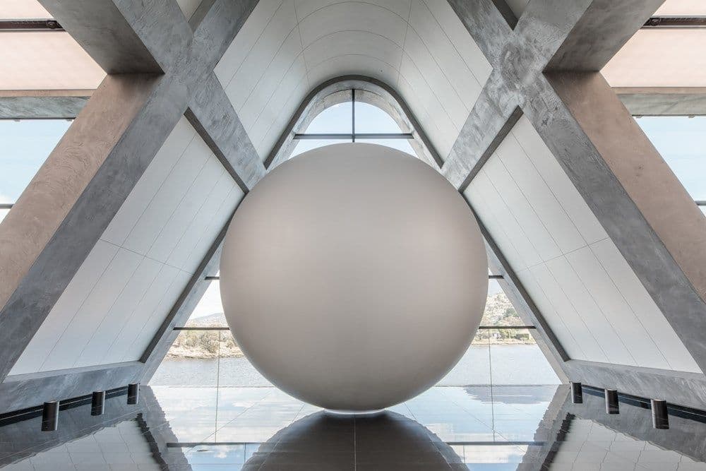 A large white sphere sits on a reflective floor in a triangular room.